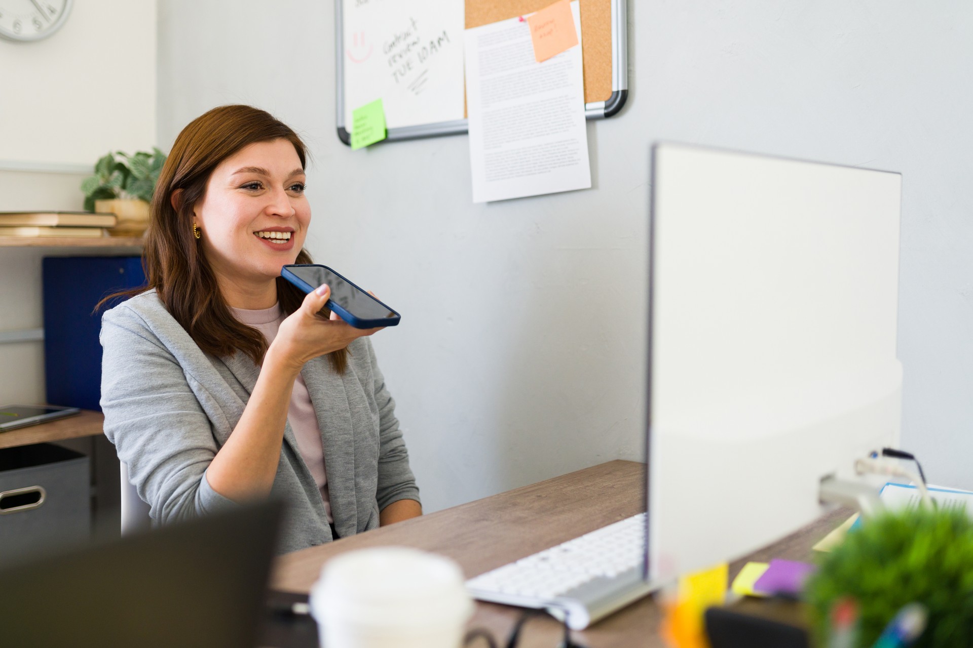 Young businesswoman confidently recording a voice note on her smartphone in a modern office setting